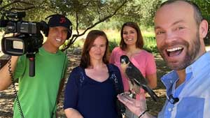 Rob, right, holds a haw in his outstretched hand, with two women behind him and a man holding a camera.