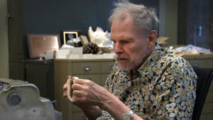 Prof Geerat Vermeij sits at his desk, examining a seashell with his hands