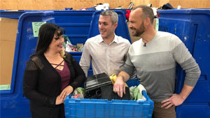 Rob stands with a man and a woman in front of a donation 