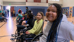 Two children smile at the camera from a line of children in wheelchairs.