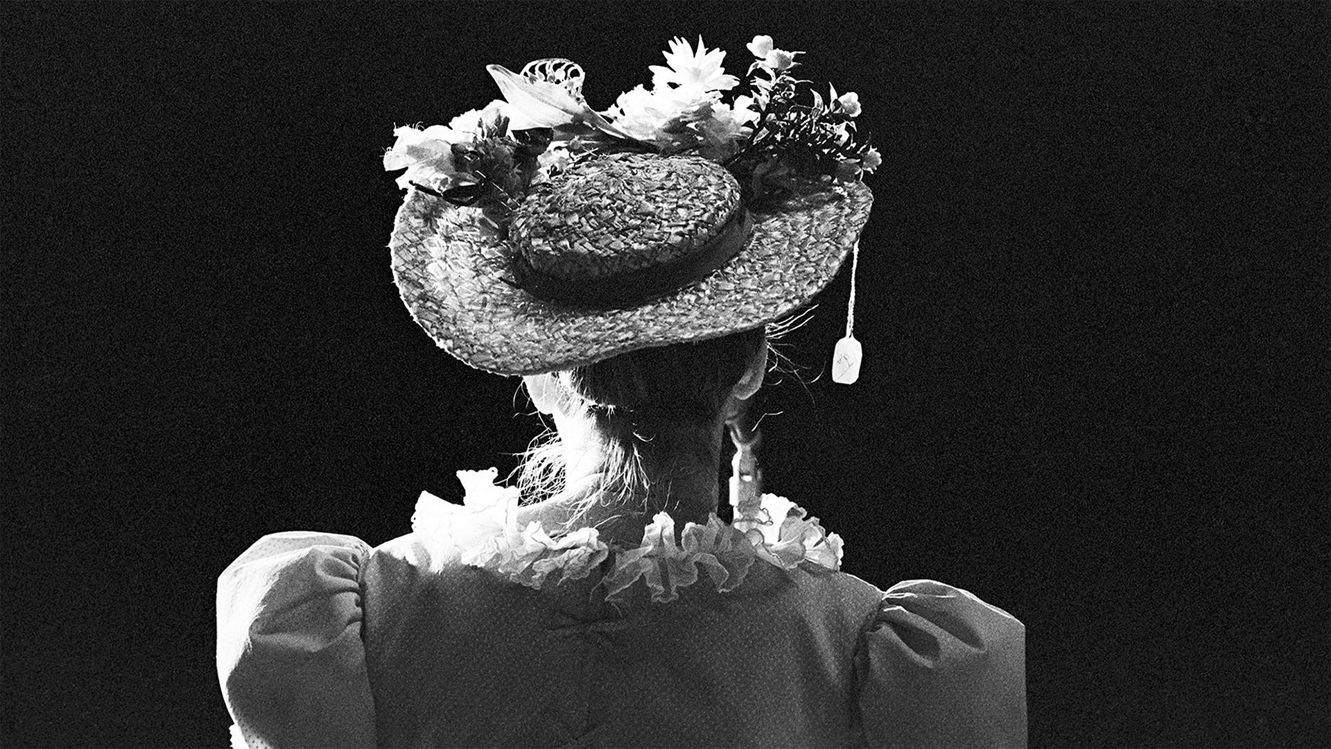 A woman, with her back to the camera, is wearing a straw hat with a price tag noticeably hanging from the brim. 