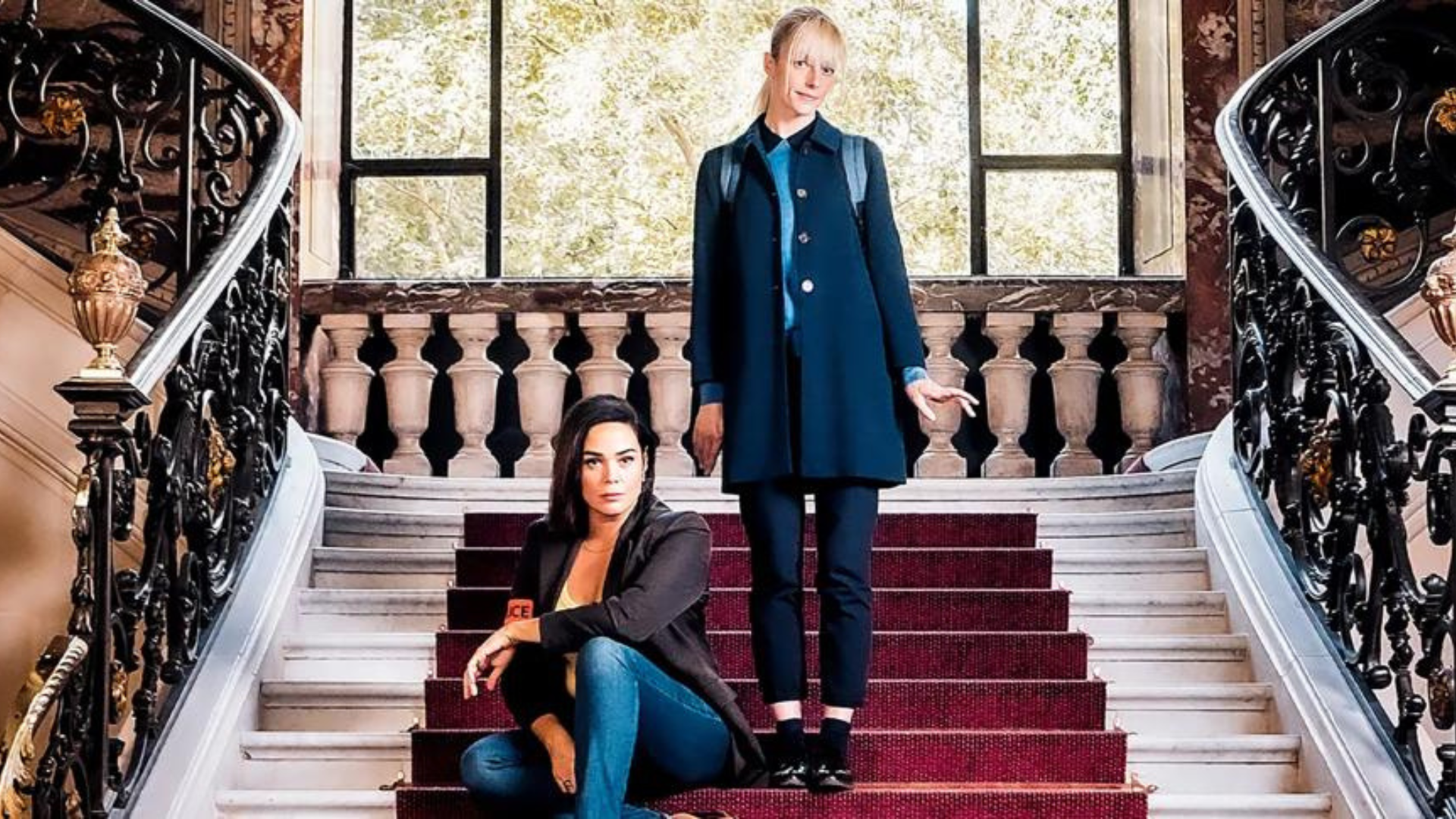 From left, inspector Raphaëlle Coste is sitting on a flight of ornate marble stairs with Astrid Nielsen standing next to her. 