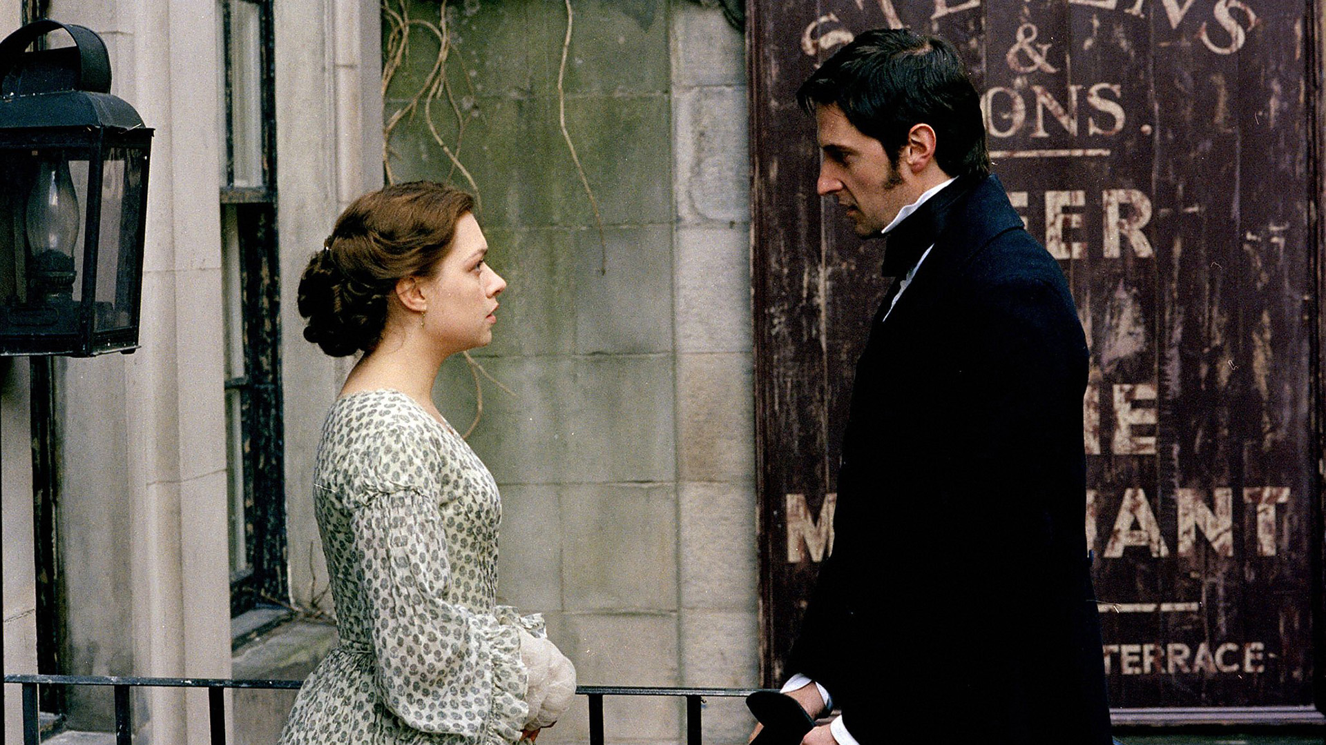 Margaret Hale and John Thornton speaking and gazing at each other in front of an industrial building. 